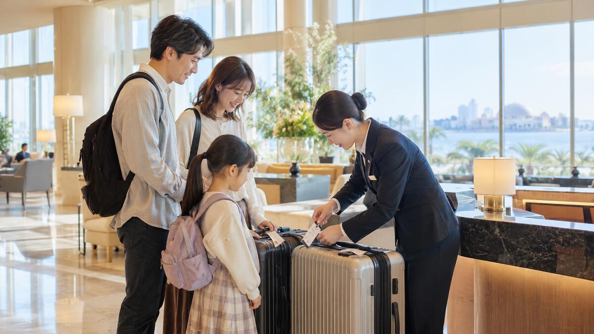 ホテルのフロントで、帰り便に向けてスーツケースに配送伝票を付けてもらう家族連れ。