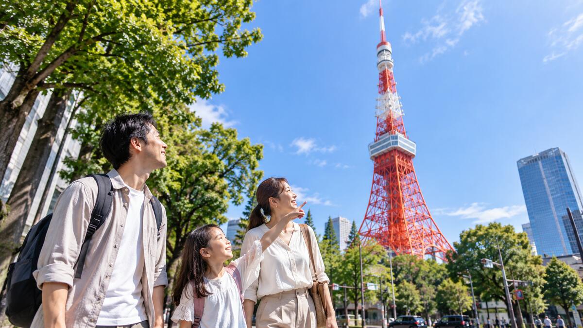 A family looking up at Tokyo Tower from the tree-lined path in Shiba Park.