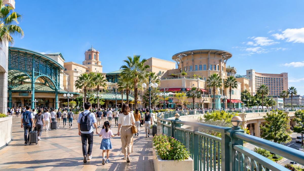 A family pulling suitcases across the resort-style plaza in front of Maihama Station, Ikspiari's buildings in the background.